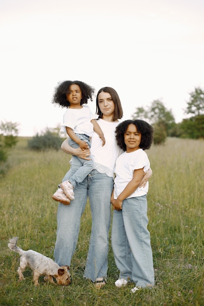 Foto der kaukasischen Mutter und zwei ihrer afroamerikanischen Töchter, die sich im Freien umarmen. Mädchen hat schwarzes lockiges Haar