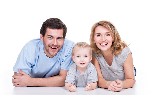 Foto der lächelnden jungen Eltern mit dem kleinen Kind, das auf dem Boden liegt - lokalisiert