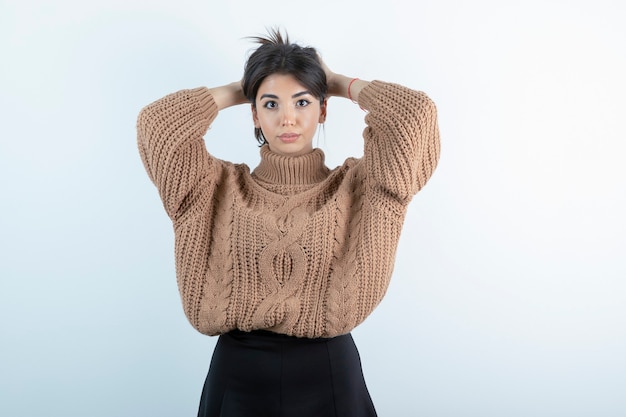 Foto der schönen Frau im gestrickten Pullover, der ihr Haar auf weißem Hintergrund hält.