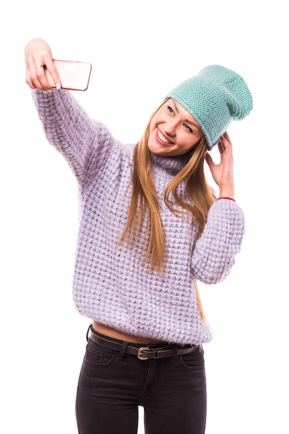 Foto der stilvollen hübschen jungen Dame halten Telefon lächelnde klebende Zunge machen Selfies Anhänger Blogger tragen Sonne Spezifikationen lässig Hut Jacke gelber Pullover isoliert weiße Farbe Wand