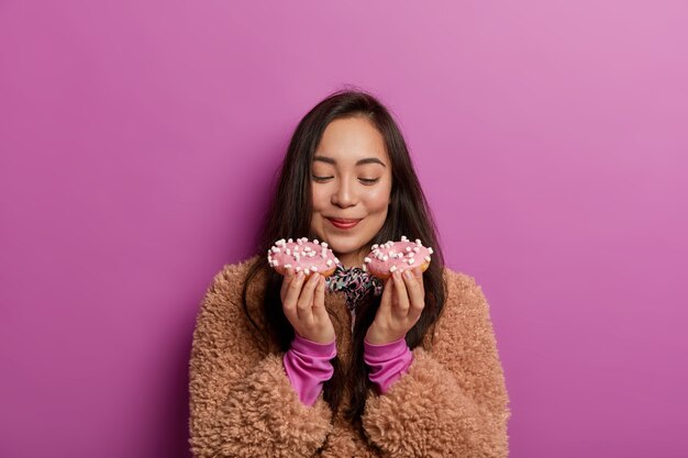 Foto der zuckersüchtigen Frau riecht frisch gebackene Donuts, unmöglich zu widerstehen, Dessert zu essen, bereit, Dessert mit gutem Appetit zu essen