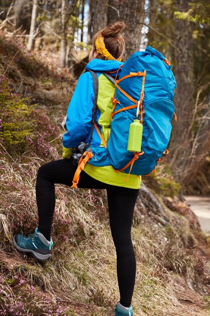 Foto des aktiven weiblichen Touristen klettert auf Hügel der Berge, trägt großen Rucksack, trägt Stiefel