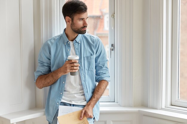 Foto des bärtigen administrativen Mamagers hält Papiere, Einweg-Tasse Kaffee