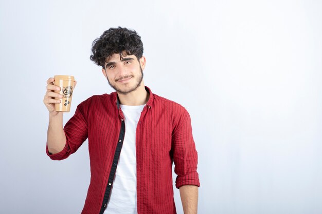 Foto des brünetten Mannes, der Tasse Kaffee für Pausenzeit über weißer Wand hält.