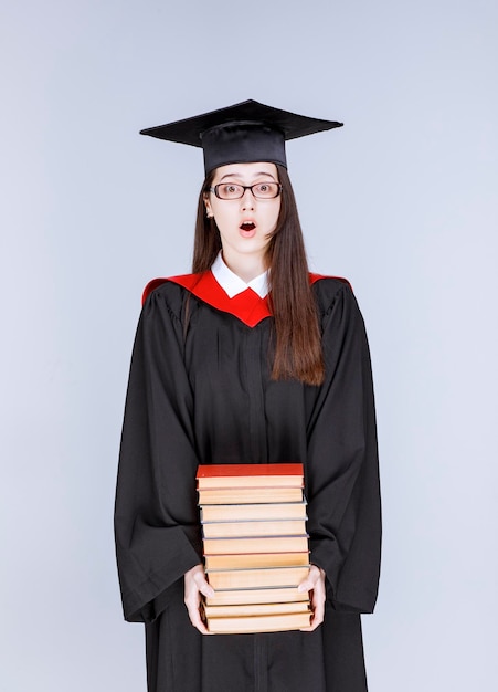 Foto des Doktoranden im Kleid, das Bücher hält. Foto in hoher Qualität