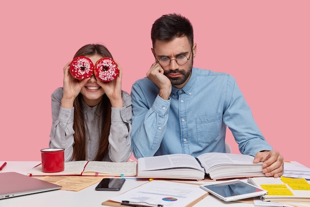 Foto des ernsthaften unrasierten Mannes trägt eine Brille für gute Sicht, gekleidetes formelles Hemd, liest aufmerksam Buch, positive weibliche Gruppenmitglied hat Spaß