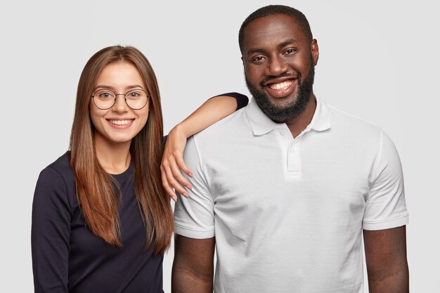 Foto des fröhlichen reizenden vielfältigen Paares lächeln positiv, stehen nebeneinander