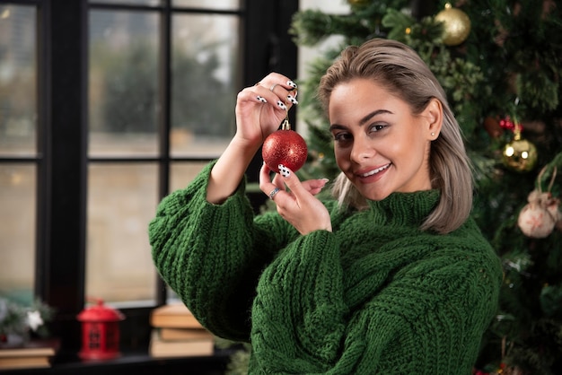 Foto des positiven Mädchens, das eine rote Weihnachtskugel hält