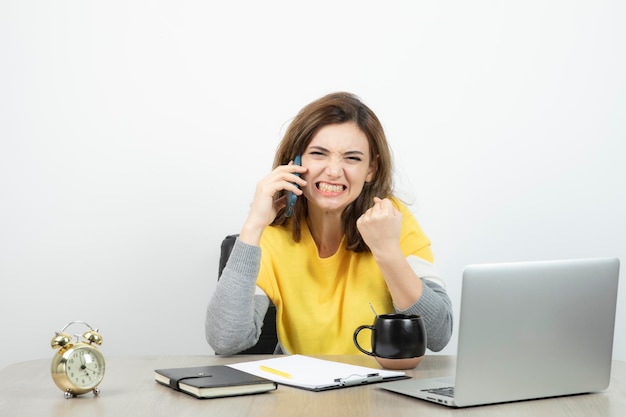 Foto einer Büroangestellten, die am Schreibtisch sitzt und mit dem Handy telefoniert. Foto in hoher Qualität