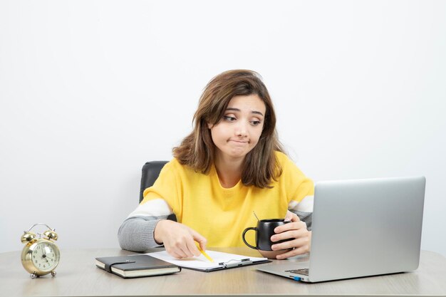 Foto einer Büroangestellten, die mit Laptop und Klemmbrett am Schreibtisch sitzt. Foto in hoher Qualität