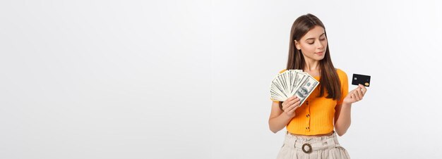 Foto einer glücklichen jungen Frau, die isoliert vor grauem Hintergrund steht und beiseite schaut und Geld und Cr hält