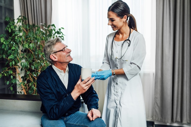 Foto einer glücklichen Ärztin, die ihrem Patienten Wasser gibt, ein Pflegeheim, eine Assistentin, Hilfe für diejenigen, die es brauchen.