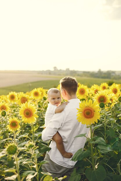 Foto einer jungen Familie am Sonnenblumenfeld an einem sonnigen Tag. Der brünette Vater und sein kleiner blonder Sohn posieren für ein Foto