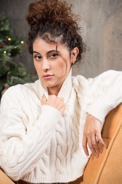 Foto einer jungen Frau, die in einem bequemen Stuhl in der Nähe des Weihnachtsbaums sitzt