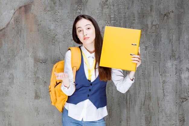 Foto einer jungen Frau mit gelbem Rucksack, der Ordner hält. Foto in hoher Qualität