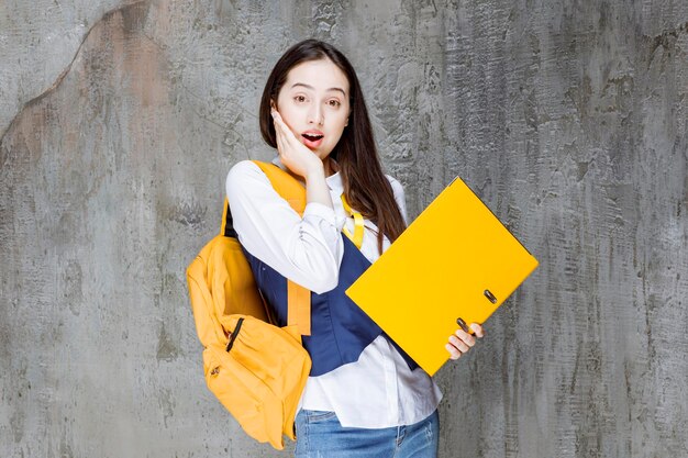 Foto einer jungen Frau mit gelbem Rucksack, die über der Mauer steht. Foto in hoher Qualität