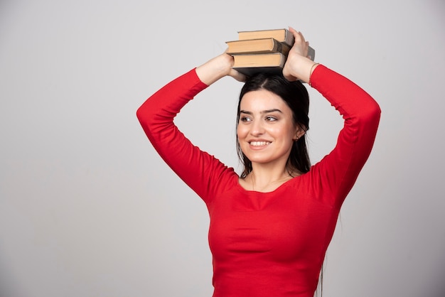 Foto einer lustigen Frau, die Bücher obenliegend hält.