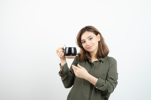 Foto eines entzückenden jungen Mädchens, das eine Tasse heißen Kaffee hält. Foto in hoher Qualität