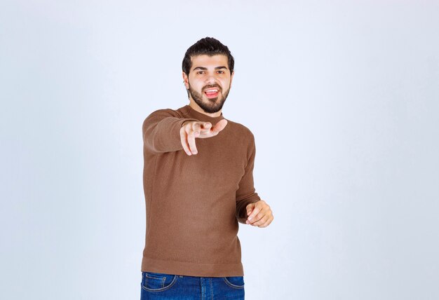 Foto eines jungen attraktiven Modells in der braunen Strickjacke, die auf weißer Wand aufwirft. Foto in hoher Qualität