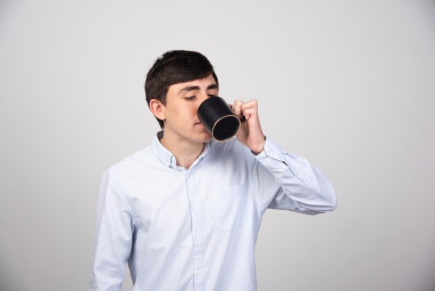 Foto eines jungen gutaussehenden Mannes, der aus einer Tasse trinkt