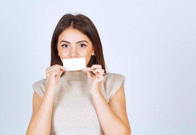 Foto eines Modells der jungen Frau, das ihren Mund mit einer Karte bedeckt und aufwirft.