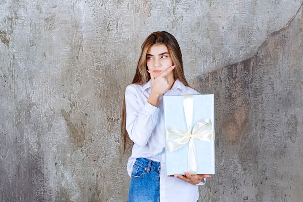 Foto eines nachdenklichen Models mit langen Haaren, das ein großes Geschenk hält