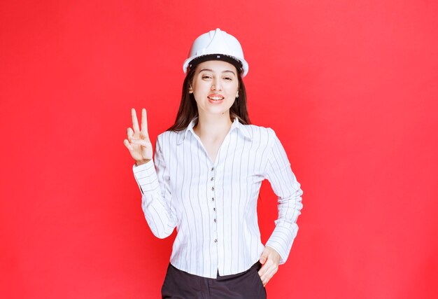 Foto eines tragenden Sicherheitshutes der schönen Geschäftsfrau, der Victory-Zeichen zeigt.