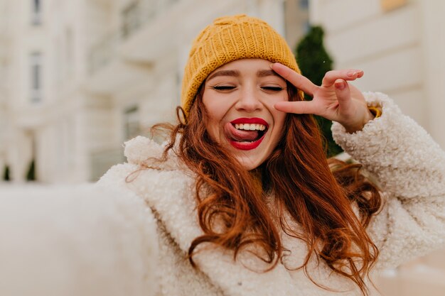 Foto im Freien des lächelnden erstaunlichen Mädchens, das Winter genießt. Attraktives weibliches Modell des Ingwermodells, das Selfie macht.