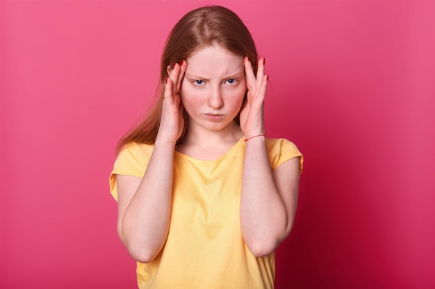 Foto in halber Länge von einem traurigen Teenager-Mädchen mit schrecklichen Kopfschmerzen, hat ernsthafte Probleme in der Schule, trägt sich lässig und posiert auf Pink. Gesichtsausdrücke und Menschen Emotionen Konzept.