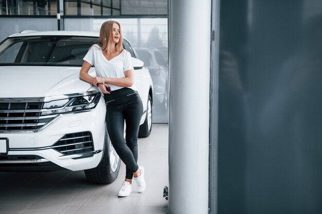 Foto in voller Länge. Mädchen und modernes Auto im Salon. Tagsüber drinnen. Neues Fahrzeug kaufen