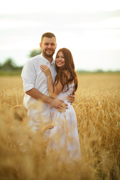 Foto in voller Länge von einem romantischen Paar in weißer Kleidung, das sich bei Sonnenuntergang im Weizenfeld umarmt.