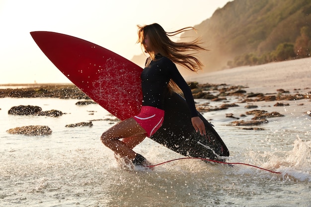 Foto von aktiven Surfer springt vor Glück ins Wasser, hat Zeit für ihr Lieblingshobby