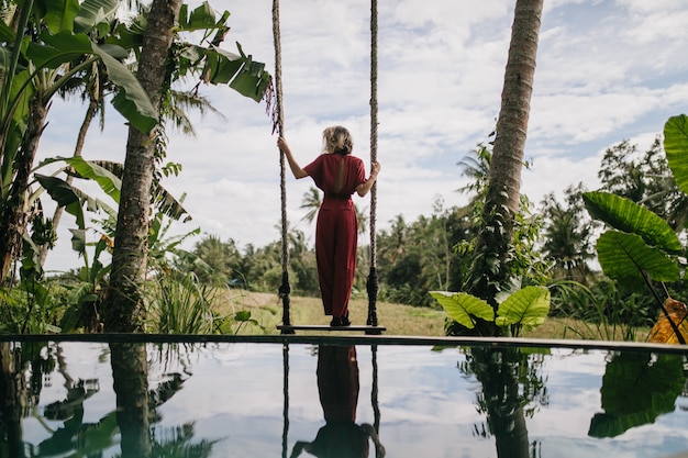 Foto von der Rückseite der schlanken Frau im langen Kleid, das regnerischen Himmel betrachtet. Außenaufnahme des formschönen weiblichen Modells, das Naturansichten am Resort genießt.