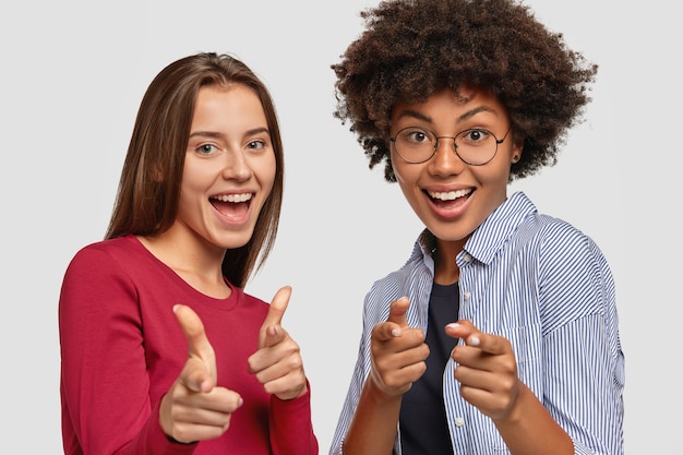 Foto von freudigen verschiedenen Frauen machen Waffengeste direkt, lächeln glücklich