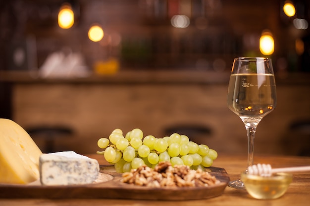 Foto von frischen Trauben neben einem Weinglas auf einem Holztisch. Verkostung von französischem Käse. Leckere Walnüsse.