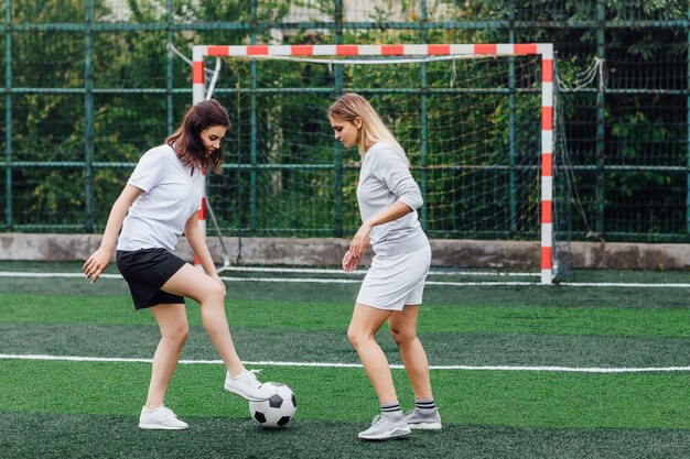 Foto von zwei hübschen Frauen, die zusammen auf dem Feld Fußball spielen