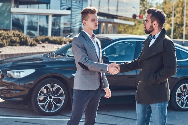 Foto von zwei smarten, eleganten Männern, die einen Auto-Deal haben. Sie machen Händedruck.