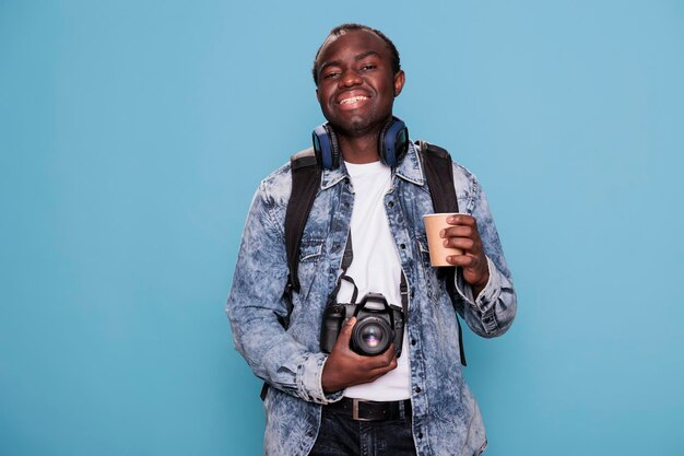 Fotoenthusiast mit DSLR-Gerät und Reiserucksack, der sich auf die Urlaubsreise vorbereitet. Herzlich lächelnder junger Mann mit Reiserucksack und professioneller Kamera, die in den Wochenendurlaub geht.