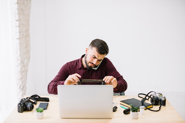 Fotograf, der Laptop bei der Unterhaltung durch Handy verwendet