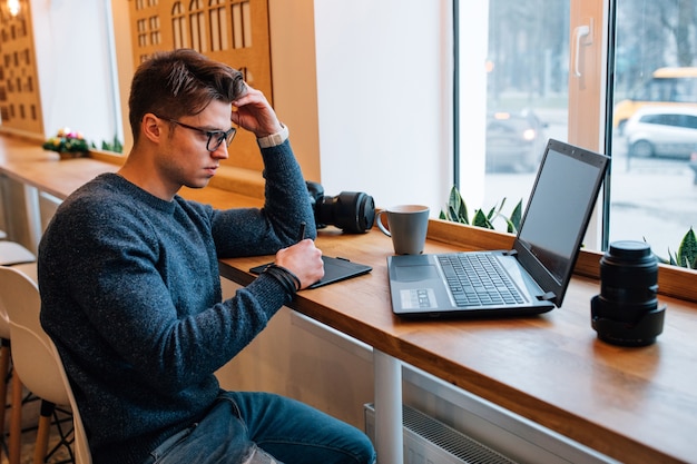 Fotograf in den Brillen, die mit interaktiver Stiftanzeige beim Betrachten des Laptops arbeiten