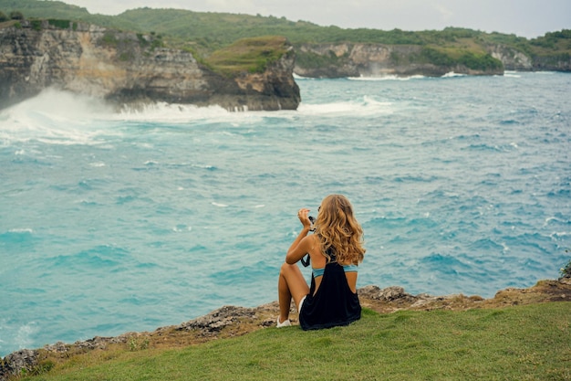 Fotografin der jungen Frau mit einer Kamera am Rand einer Klippe fotografiert die Natur