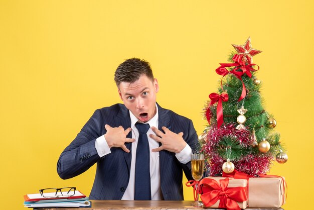 fragte sich ein Mann, der die Hände an seine Brust legte und am Tisch in der Nähe des Weihnachtsbaums saß und auf Gelb präsentierte