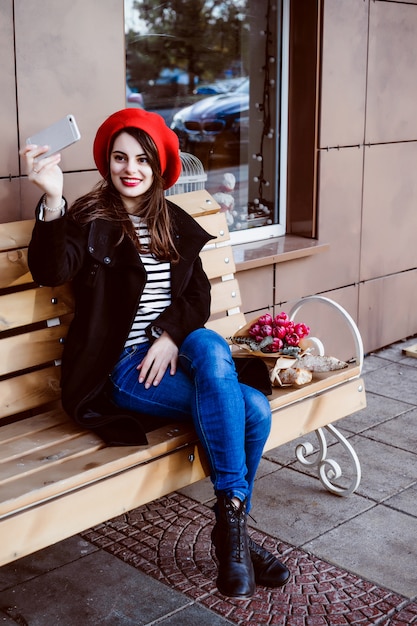 Französische Frau in einem roten Barett auf einer Straßenbank