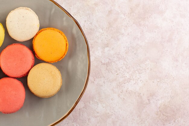 Französische Macarons der Draufsicht innerhalb der Platte auf dem rosa Tischkuchen-Kekszuckersüß