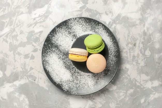 Französische Macarons der Draufsicht innerhalb der Platte auf weißem Oberflächenkuchenzucker-Backkeks-süßem Tee-Keks