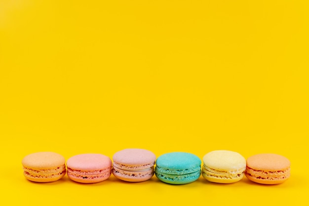 Französische Macarons der Vorderansicht bunt köstlich und gebacken auf gelbem, Kuchenkeks-Süßwaren