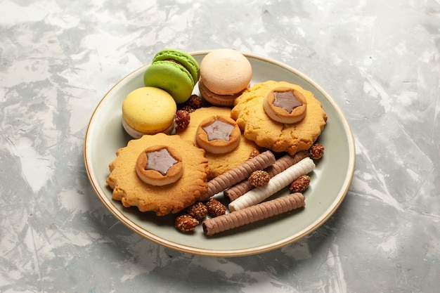 Französische Macarons der Vorderansicht mit kleinen Kuchen und Keksen auf weißer Oberfläche