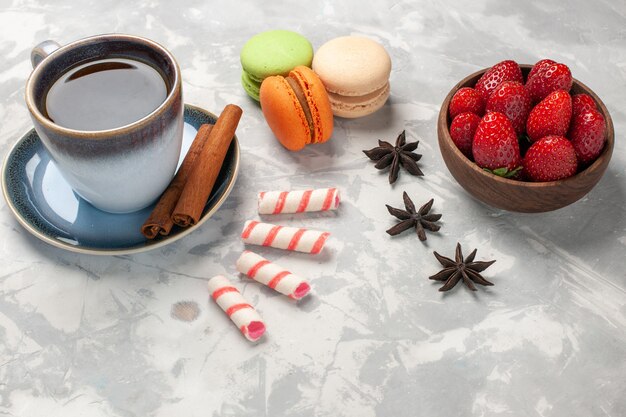 Französische Macarons der Vorderansicht mit Tasse Tee und frischen roten Erdbeeren auf süßen Keksen des weißen Oberflächenkuchenzuckerkekses