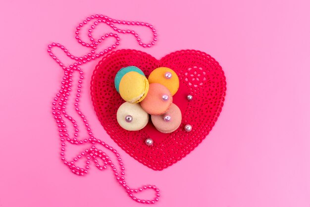 Französische Macarons mit Draufsicht runden köstlich zusammen mit roter herzförmiger Form auf rosa Kuchenkuchenkeks süß ab