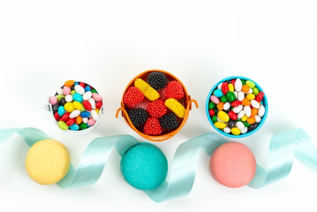 Französische Macarons mit Draufsicht zusammen mit bunten Bonbons und Marmeladen auf weißer Kuchenkeksfarbe